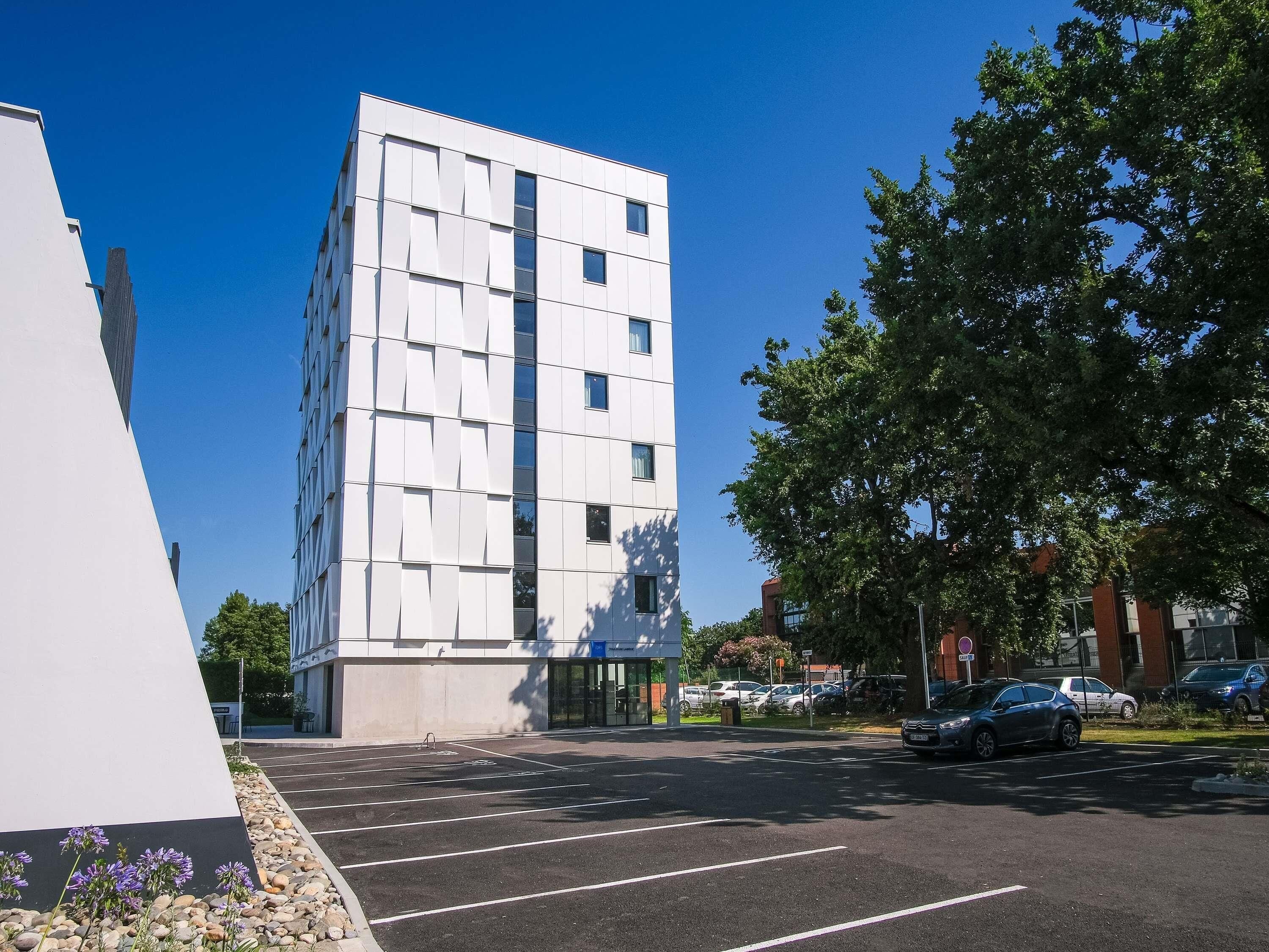 A modern building with a flat facade, multiple windows, and a parking lot with cars.