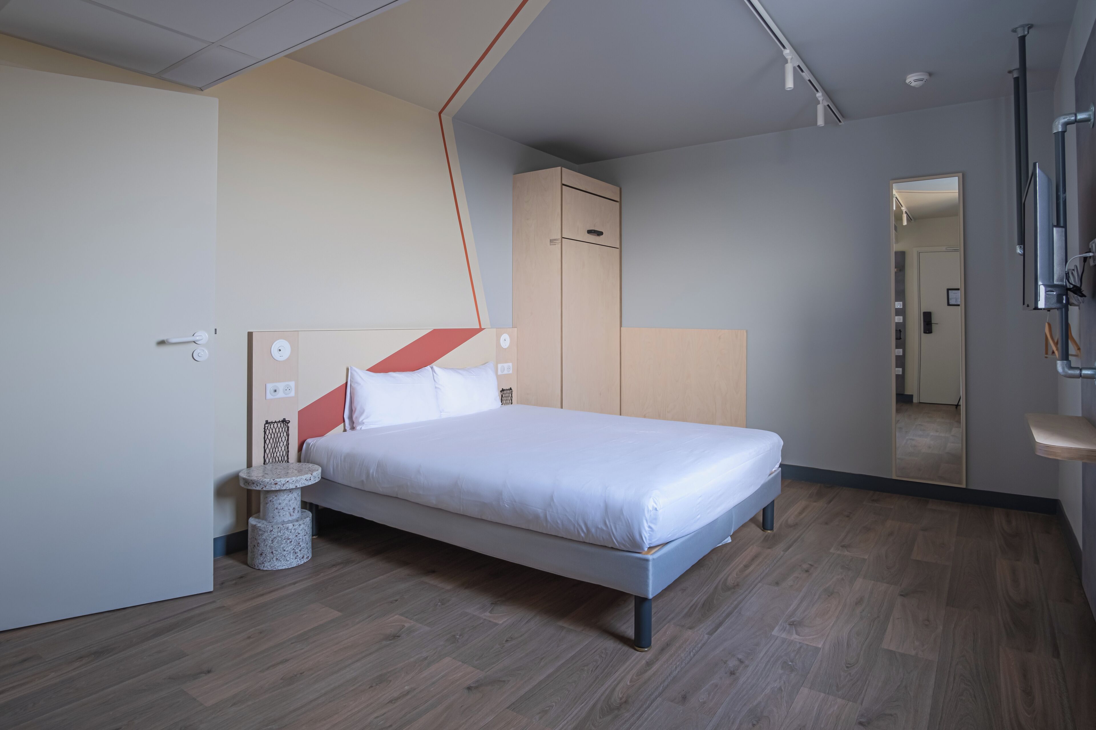 A modern bedroom with a bed, a small side table, a wardrobe, and a mirror.