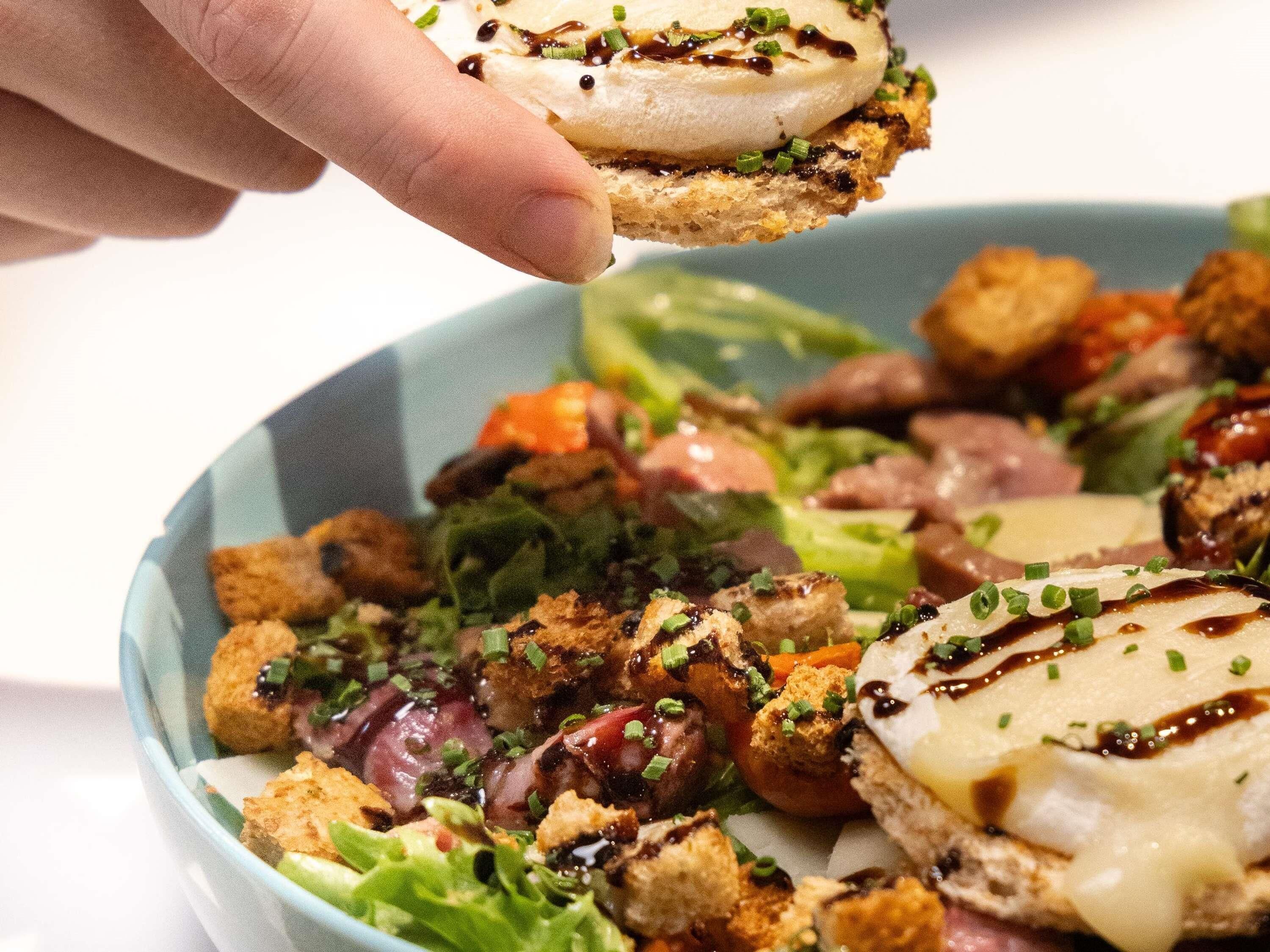 A bowl of salad with croutons and a piece of bread with cheese and sauce.
