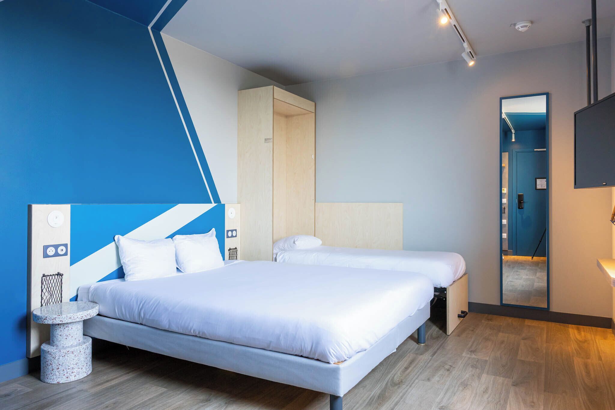 Et moderne hotelværelse med to senge, et rundt bord og et spejl.