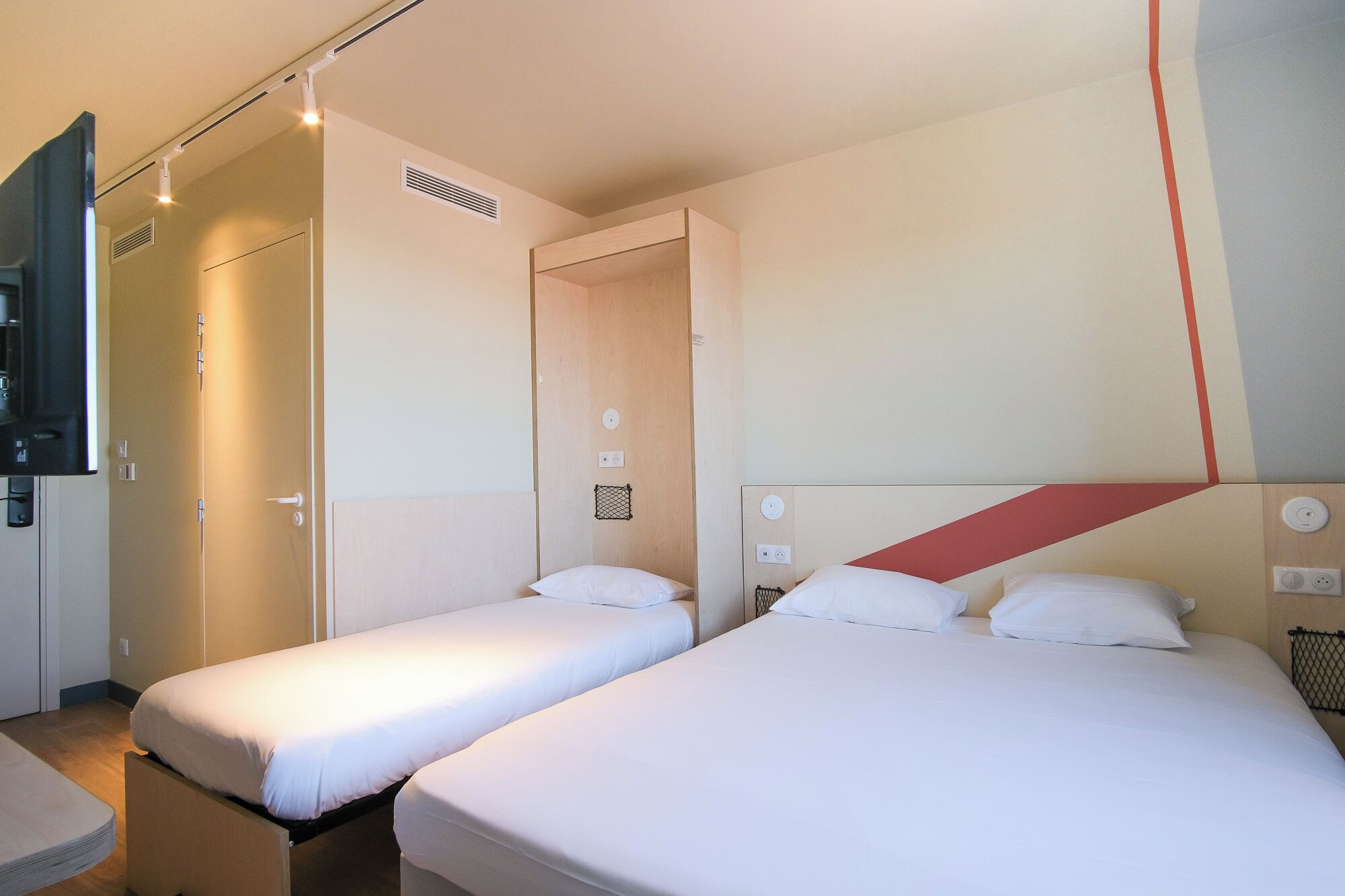 A hotel room with two single beds, a small desk, a chair, a TV, and a wardrobe.