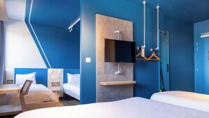 Una habitación de hotel moderna con dos camas, un televisor de pantalla plana montado en la pared, un escritorio con una silla y una mesita pequeña.