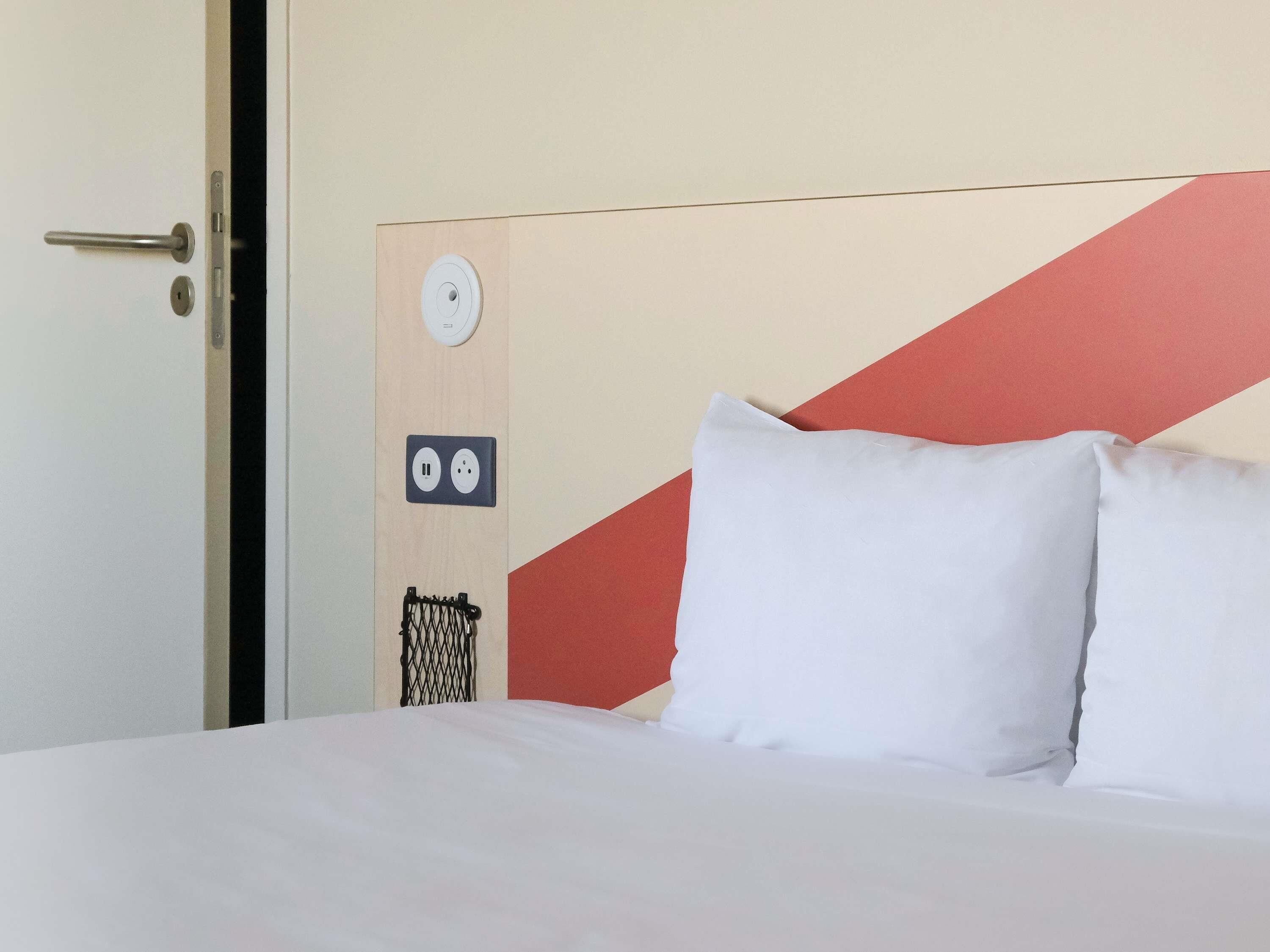 Une chambre d’hôtel avec un lit, une porte, une prise de courant fixée au mur et un interrupteur.
