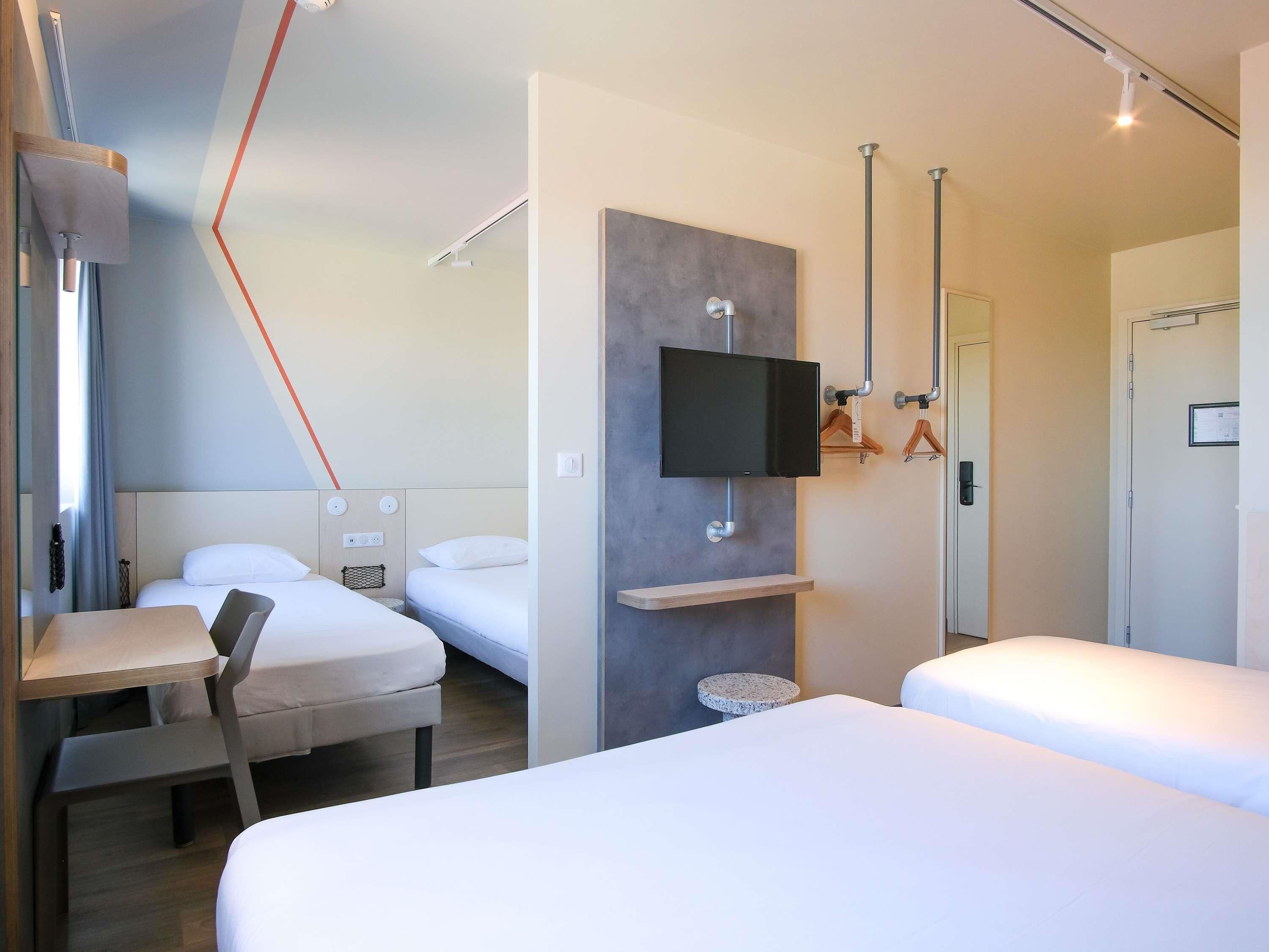 Una habitación de hotel con cama, escritorio, silla, televisor montado en la pared y puerta.