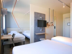 Una habitación de hotel con cama, escritorio, silla, televisor montado en la pared y puerta.