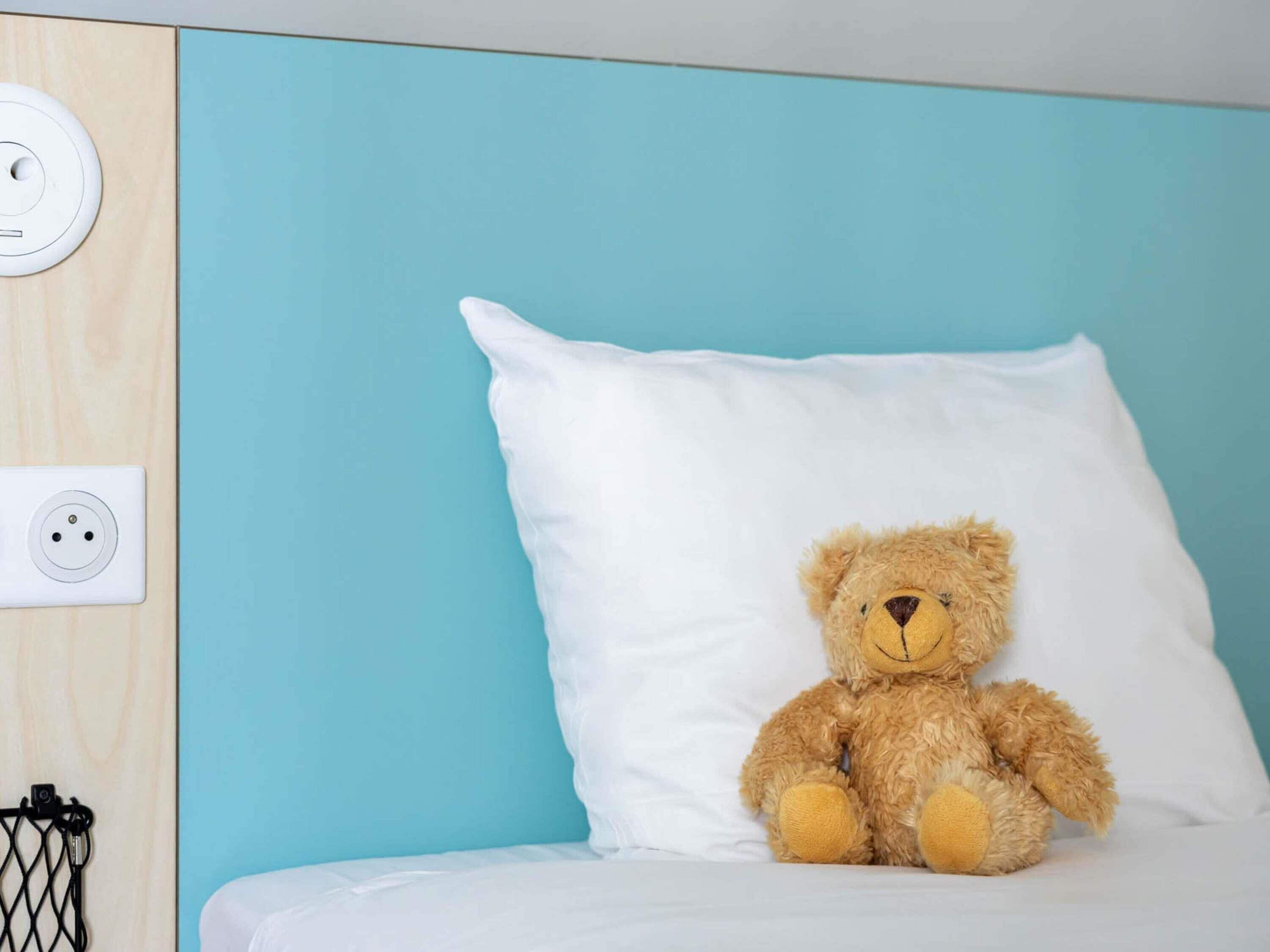 A bed with a white pillow and a teddy bear.