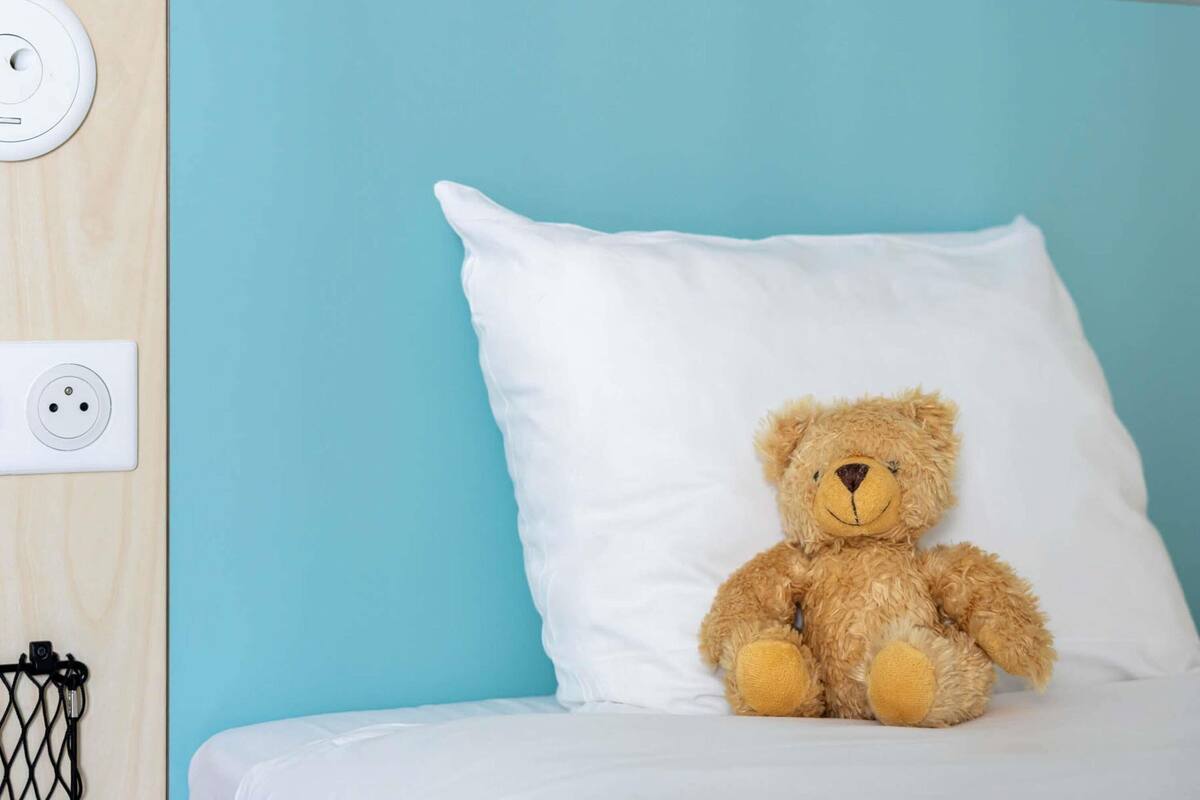 Una cama con un almohadón blanco y un osito de peluche.