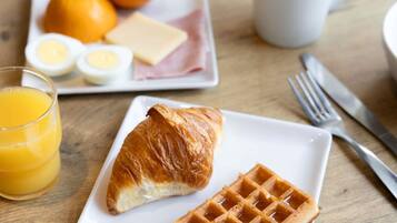 Prato de café da manhã com croissant, waffle, laranja, ovos, queijo e presunto.