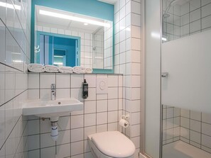 Un baño con lavamanos blanco, inodoro, espejo y zona de ducha.