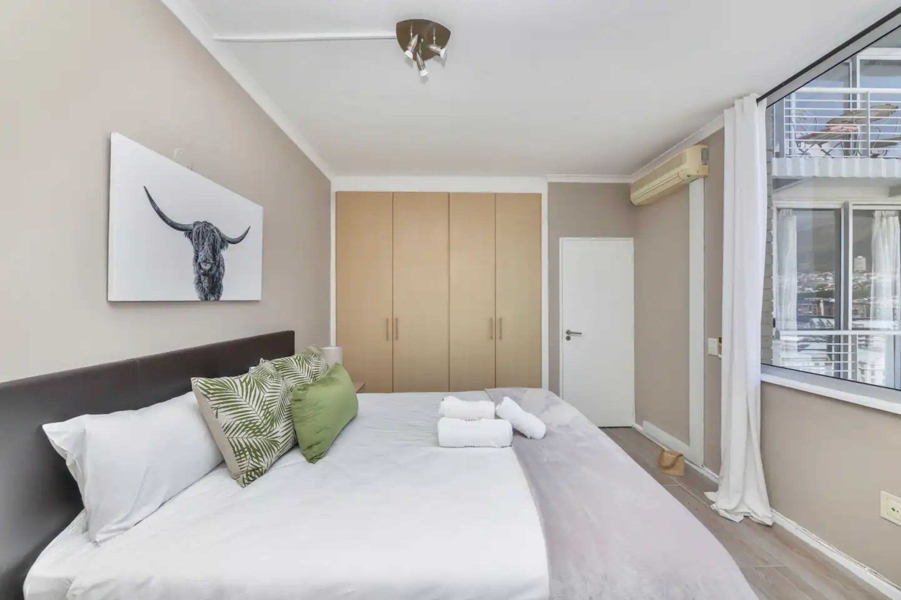A bedroom with a bed, a large window, a ceiling fan, and a wardrobe.
