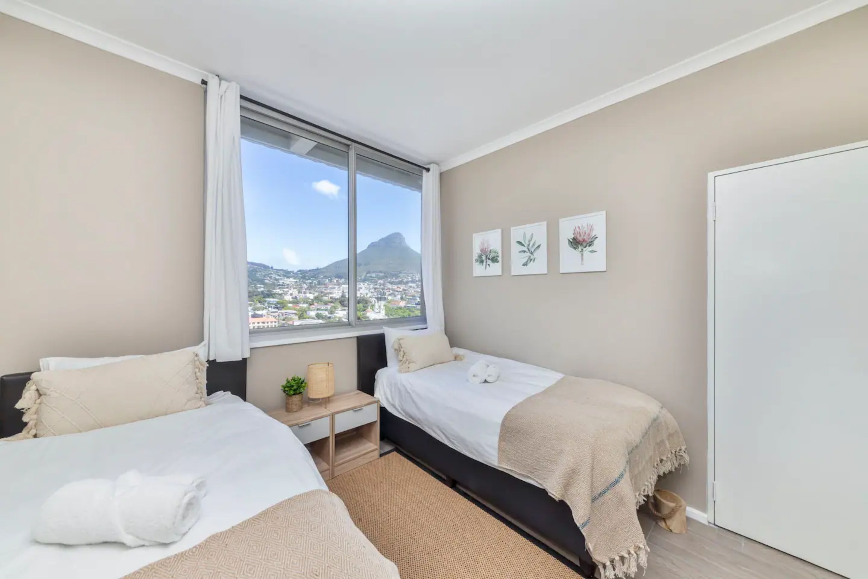 A bedroom with two beds, a window with a view of a mountain, and three framed pictures on the wall.