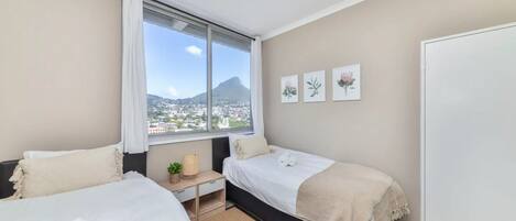 A bedroom with two beds, a window with a view of a mountain, and three framed pictures on the wall.