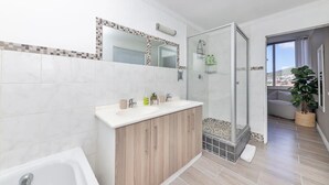 A modern bathroom with a glass shower enclosure, a white bathtub, and a wooden vanity with a mirror. - Picturesque 2BD Apartment With Table Mountain View (Cape Town)