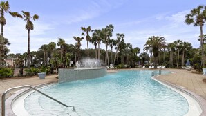 Ein Swimmingpool mit Springbrunnen, umgeben von Palmen und Liegestühlen.