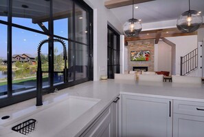 Una cocina moderna con ventanas amplias, una chimenea de piedra y vistas a una casa y un lago.