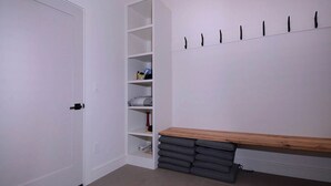 A room with a white door, a white shelving unit, a wooden bench, and a wall-mounted hook.