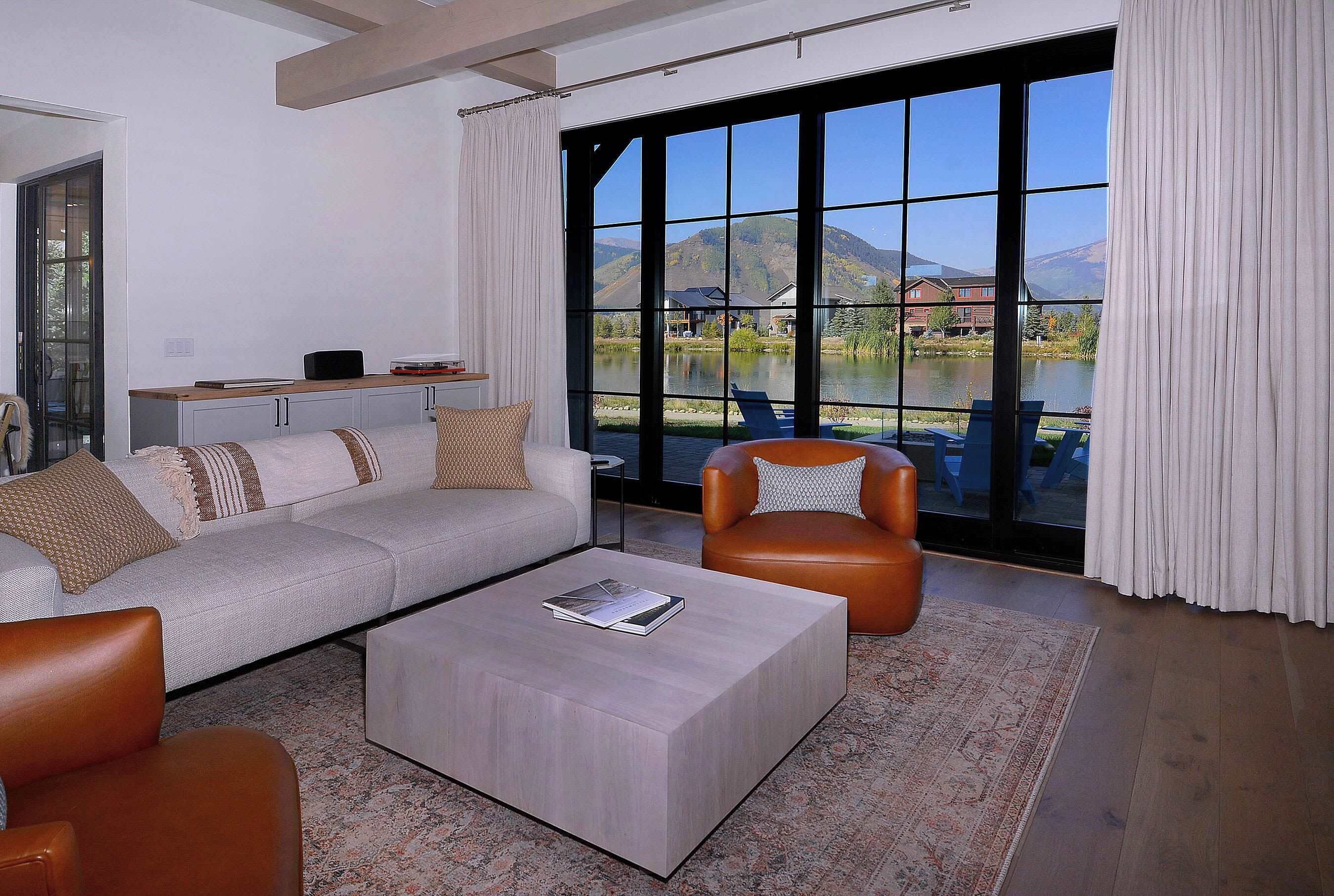 Una sala de estar moderna con un ventanal grande, un sofá, una mesa de centro y un sillón de cuero.