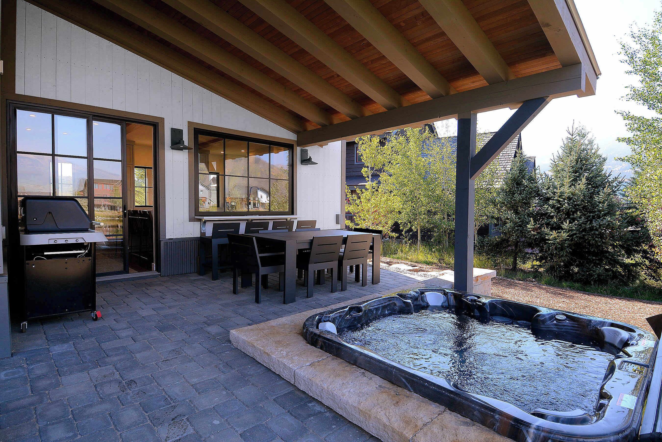 An outdoor patio with a barbecue grill, dining table, chairs, and a hot tub.