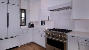 A modern kitchen with white cabinetry, a stainless steel stove, and a window overlooking the outdoors.