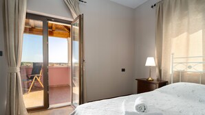 Habitación de hotel con cama, mesita de noche, lámpara, ventana con cortinas y vista al exterior.