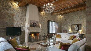 A cozy living room with a stone wall, a fireplace, a chandelier, and a television. - Exclusive luxury property with private pool in Siena countryside Borgo la Chiusa (Siena)