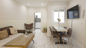 A compact living space with a sofa, a coffee table, a dining table with chairs, a kitchen area, and a TV mounted on the wall. - Recaredo, Nº4-1 bedroom apartment 2nd floor (Sevilla)