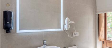 A bathroom with a large mirror, a sink, a towel rack, and a hairdryer mounted on the wall.