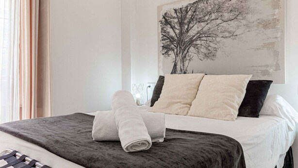 A neatly made bed with a dark grey cover, two pillows, and a folded white towel on the bed. - Recaredo, Nº4-1 bedroom apartment 2nd floor (Sevilla)
