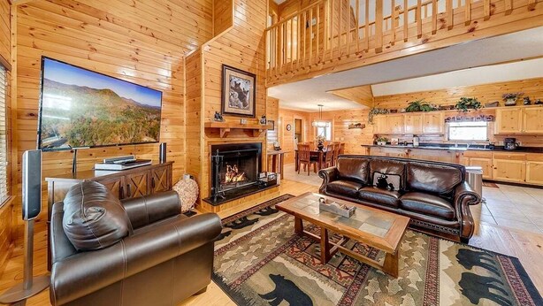 A log cabin interior with a fireplace, leather sofa, dining area, kitchen, and a staircase. - Rustic Elegance-Luxury Home Loaded with Amenities (Helen)