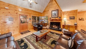 A log cabin interior with a fireplace, leather furniture, and a ceiling fan. - Rustic Elegance-Luxury Home Loaded with Amenities (Helen)
