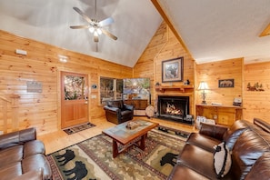 L’intérieur d’une cabane en rondins, avec une cheminée, des meubles en cuir et un ventilateur de plafond.