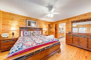 Een slaapkamer met houten lambrisering, een groot bed, een plafondventilator en een dressingkast.