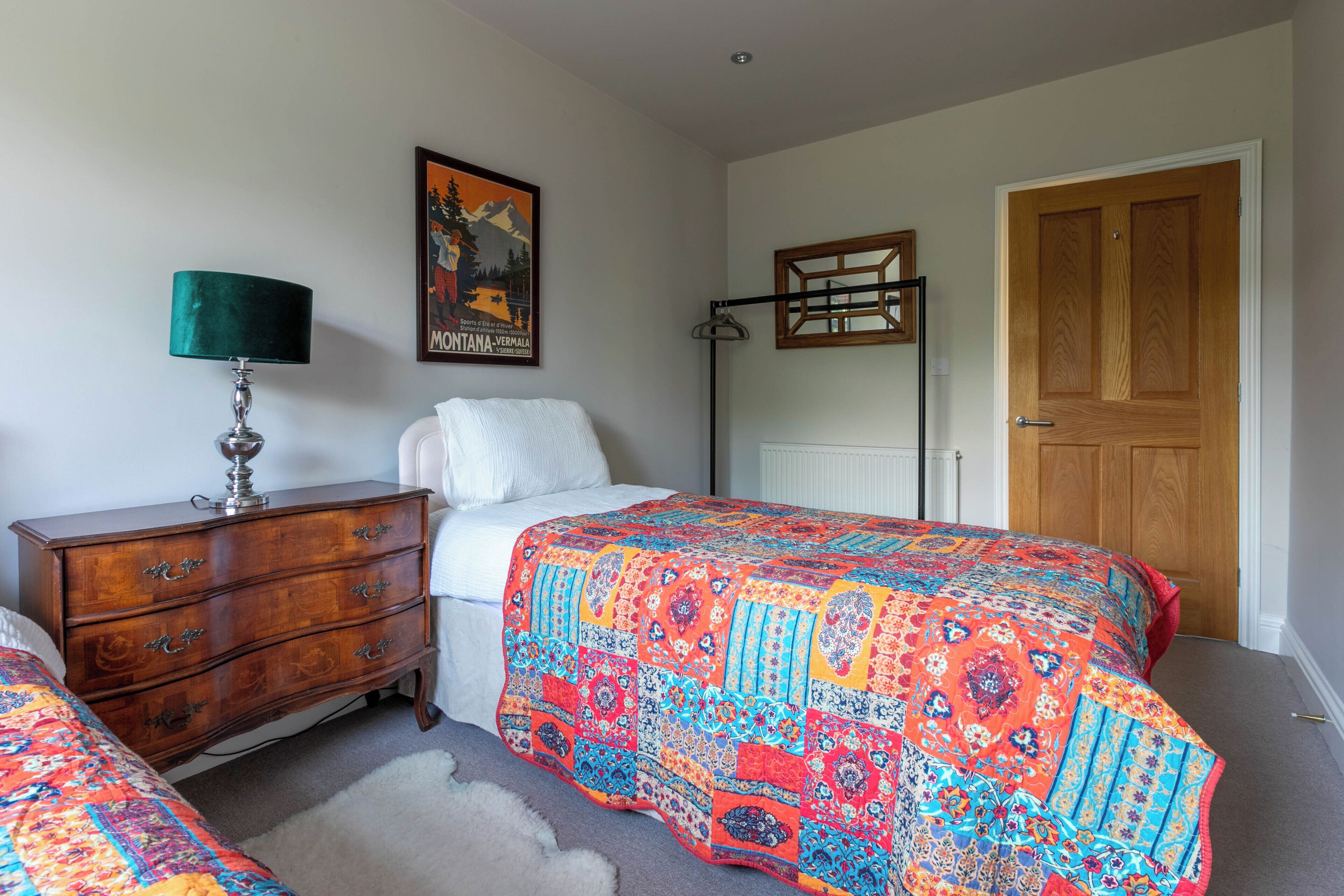 Een slaapkamer met een bed, een dressoir, een lamp, een poster en een deur.