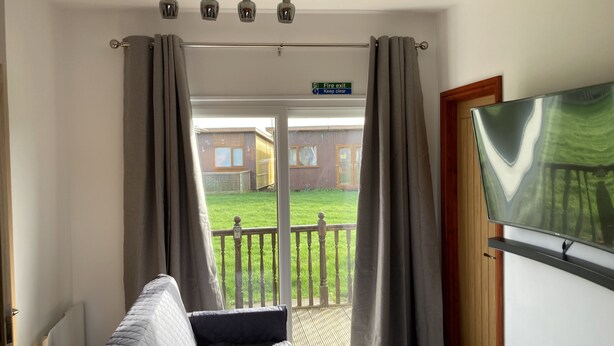 A room with a bed, a TV, and a view of a garden through a glass door. - G10 Rickardos Holiday Lets (Mablethorpe)