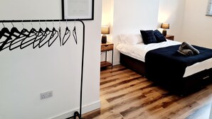 Une chambre à coucher avec un lit, des tables de chevet, une lampe fixée au mur et un tableau encadré.
