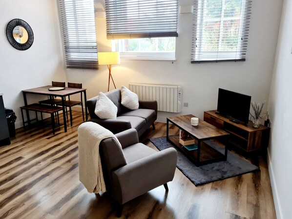 Un salon moderne comprenant un canapé, un fauteuil, une table basse, un téléviseur et un coin repas.