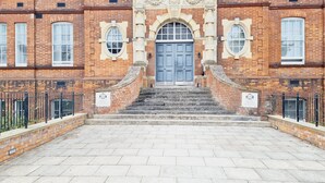 Un bâtiment doté d’une entrée centrale, avec une porte bleue, flanquée de deux fenêtres rondes et d’une arche décorative.