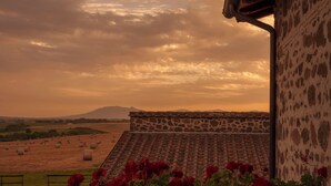 A rural landscape with hay bales, a stone building with a tiled roof, and red flowers in the foreground. - La Polledrara Relais di Campagna (Paliano)