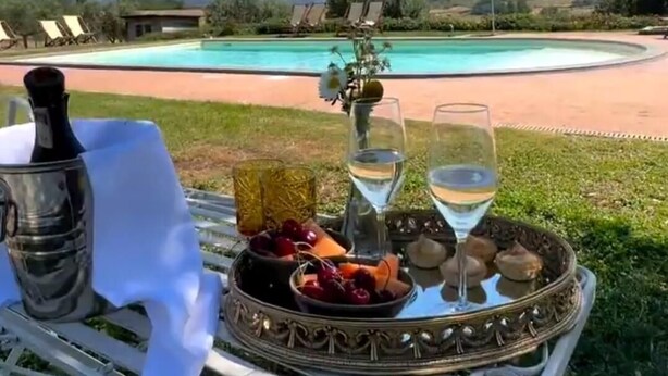 A table with a bottle, glasses, and a fruit tray overlooking a pool and mountains. - La Polledrara Relais di Campagna (Paliano)