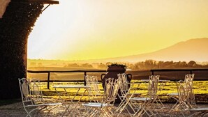 A table set outdoors with chairs and a pot, overlooking a field and mountains during sunset. - La Polledrara Relais di Campagna (Paliano)