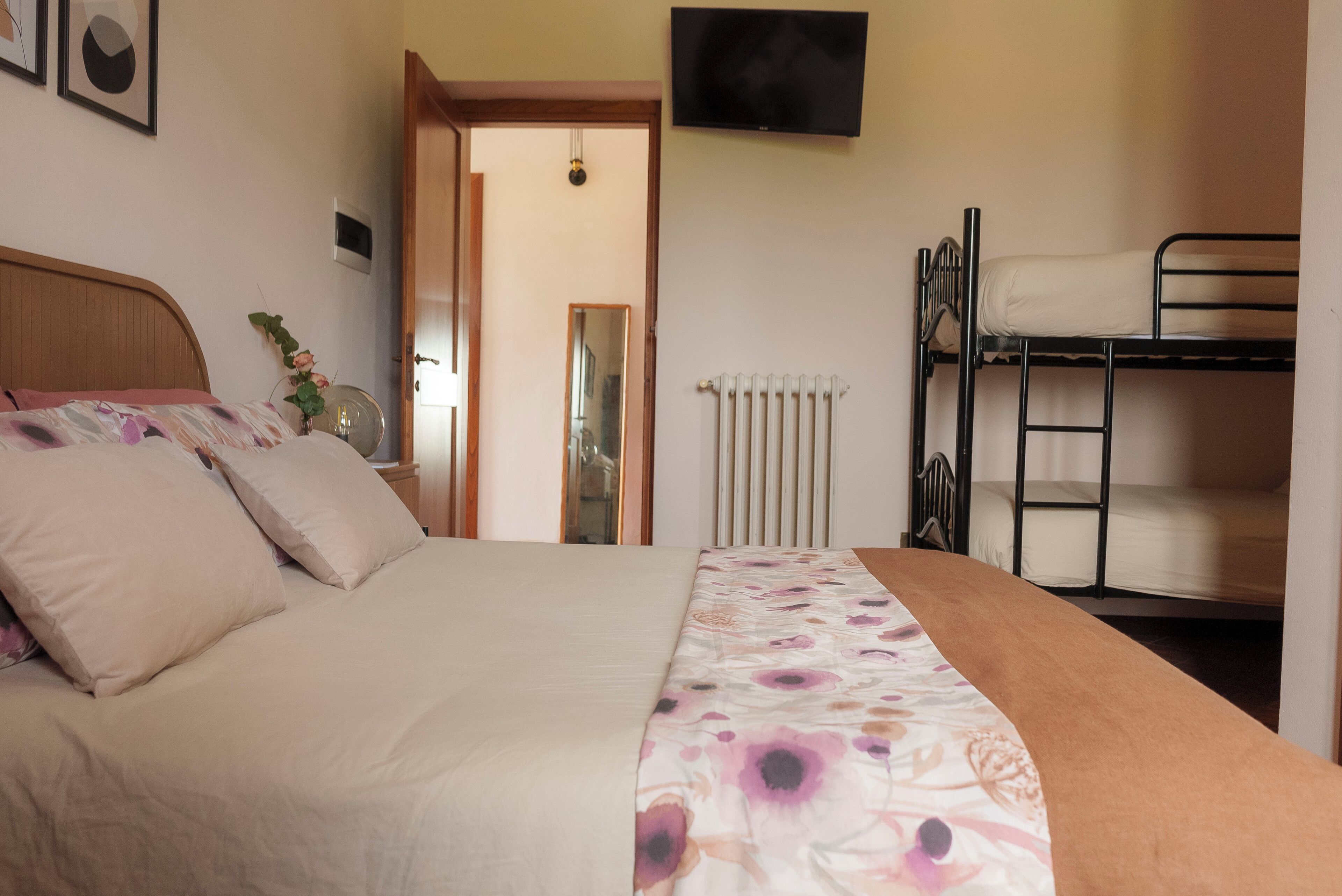 A bedroom with a bed, a bunk bed, a radiator, a TV, and a door leading to another room.