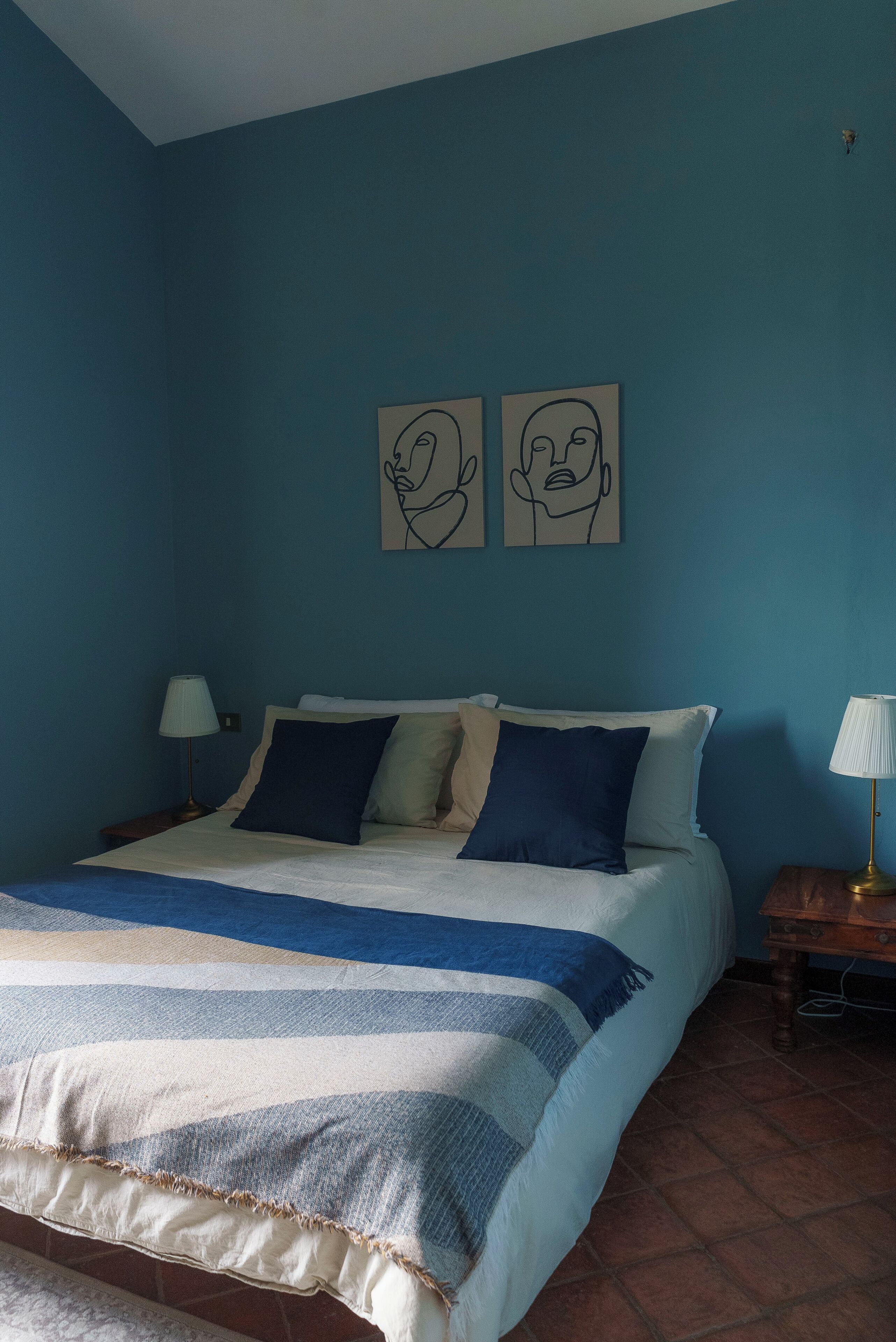 A bedroom with a bed, two wall art pieces, a nightstand, and a lamp.