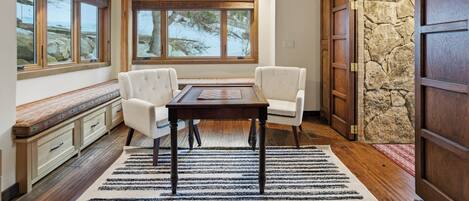 A dining area with a table and chairs, a bench with storage, large windows, and a stone wall.