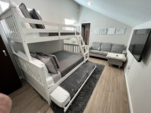A bunk bed with a grey quilt, a grey sofa, and a flat-screen TV on the wall.