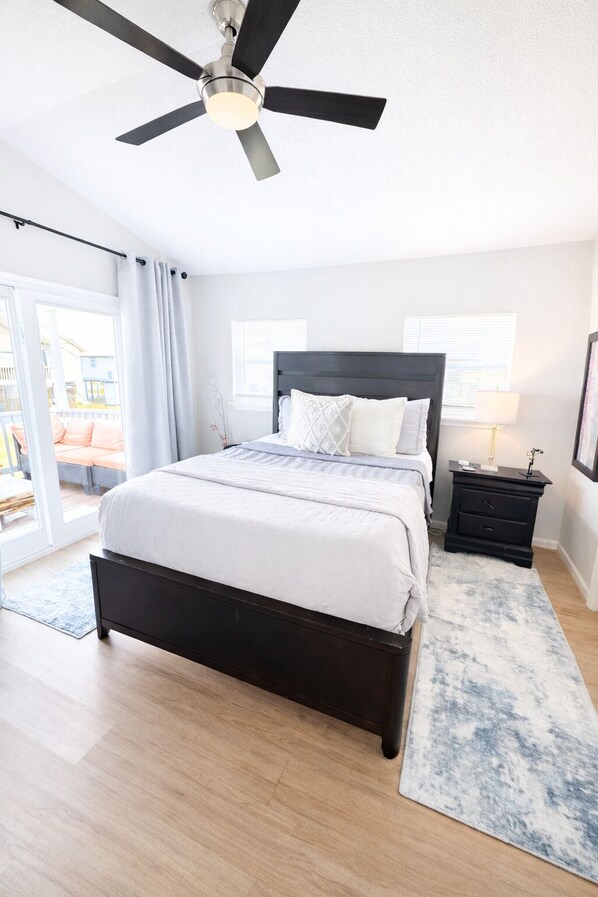 A bedroom with a bed, a nightstand, a ceiling fan, and a view of the outside. - Golf Cart/Pets Allowed/3m to Beach (Galveston)