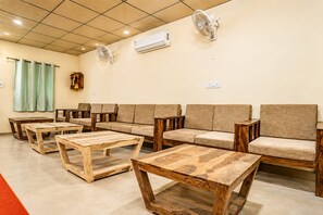 A waiting area with sofas, wooden tables, a wall-mounted air conditioner, and a ceiling fan. -  Barkha Desert Safari Camp Sam Sand Dunes (Jaisalmer)