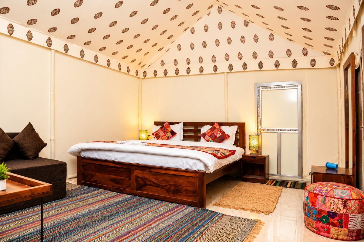 A bedroom with a bed, bedside tables, a nightstand, a sofa, a colorful rug, and a patterned ceiling.