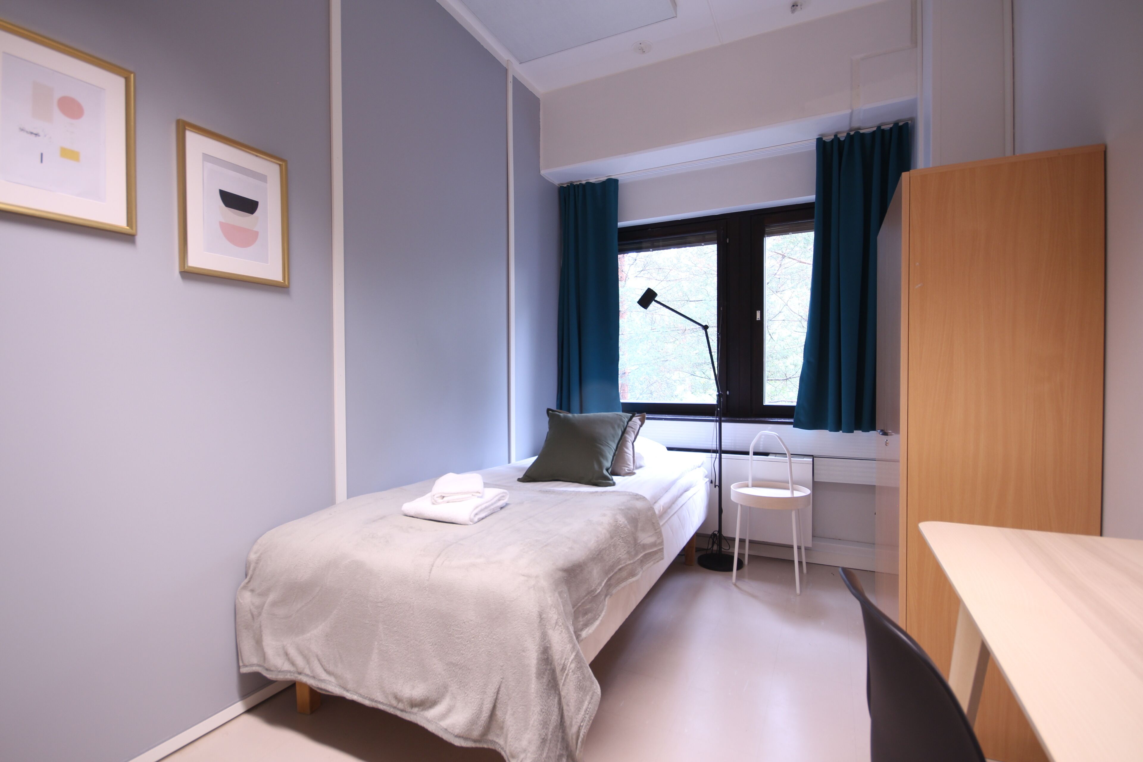 Ein modernes Schlafzimmer mit einem Bett, einem Schreibtisch, einem Stuhl und einem Fenster mit Vorhängen.
