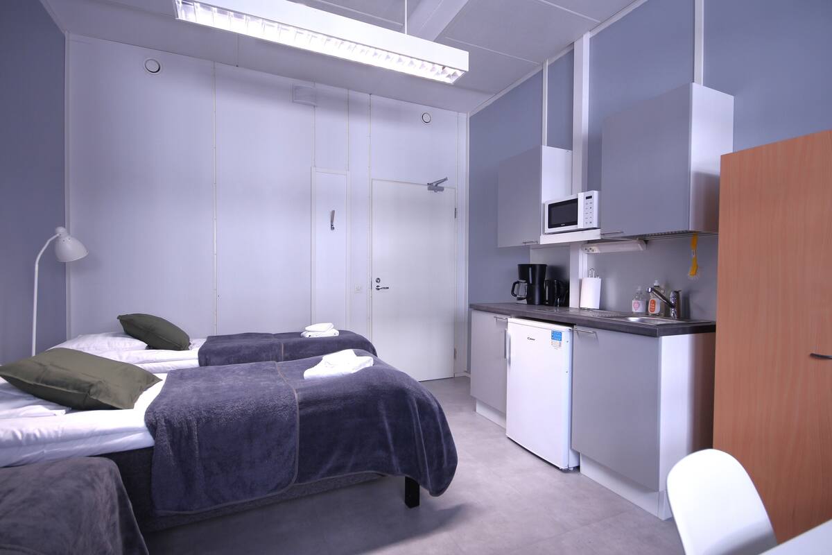 A bedroom with two beds, a small kitchenette, and a bathroom.