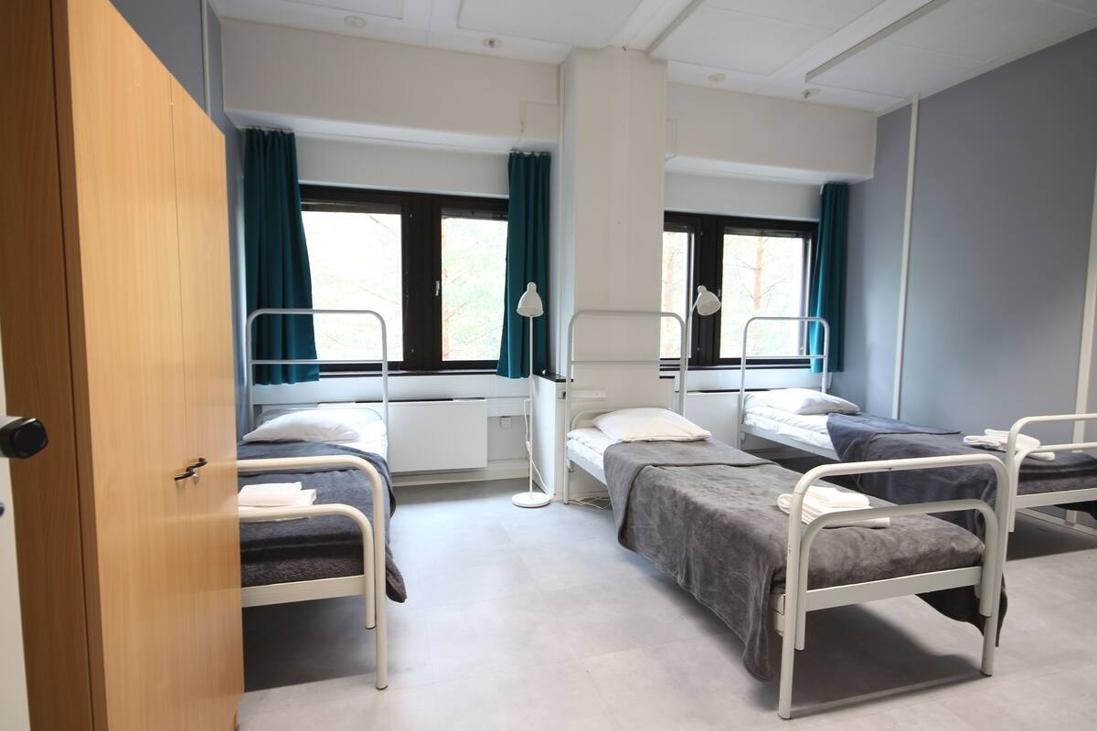 A room with three single beds, a wooden wardrobe, and a window with curtains.